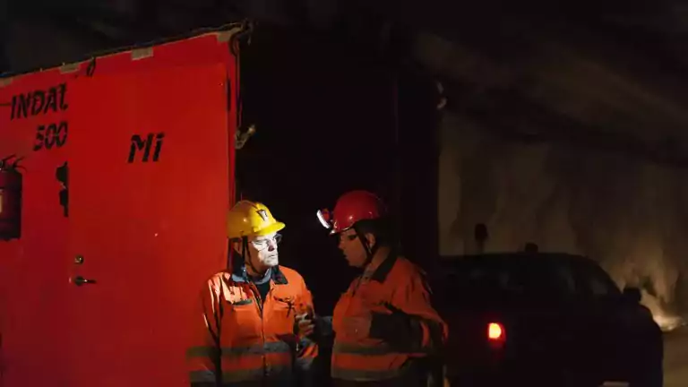 Two workers at night with headlamps talking in front of a battery storage unit