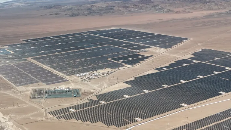 Aerial view of the AES Andes solar facility in Chile featuring extensive rows of photovoltaic panels across a desert landscape with supporting electrical infrastructure.